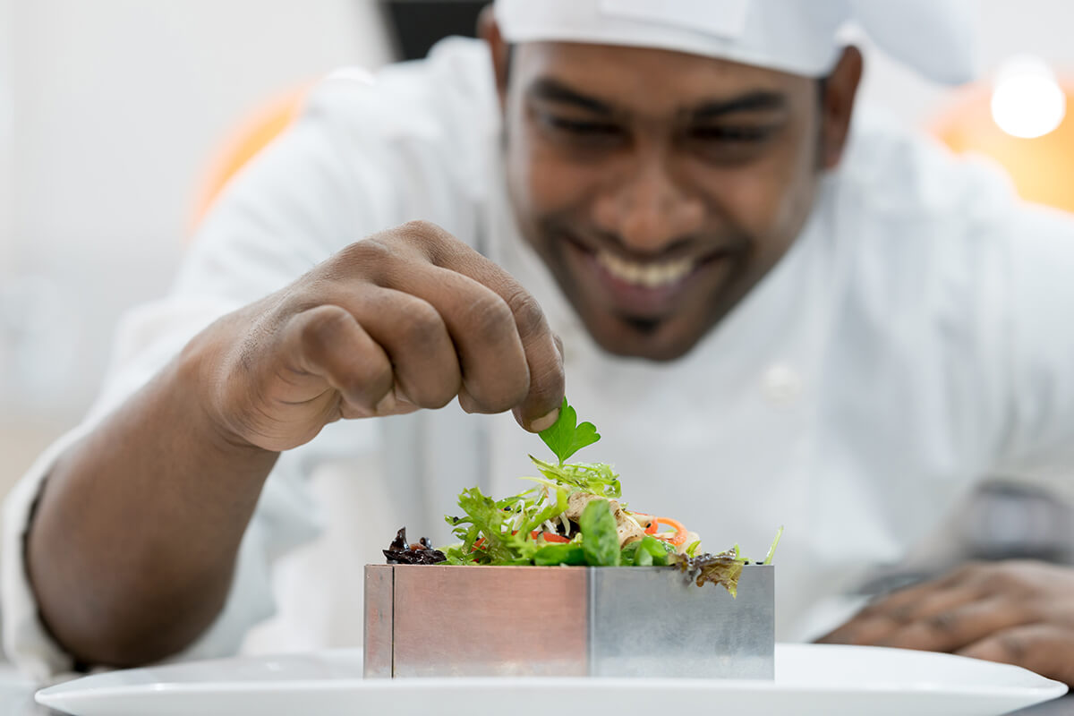 Happy indian chef adding details to his finished plate