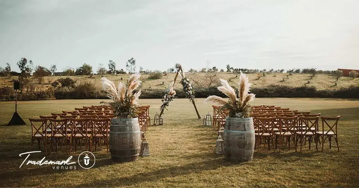 Outdoor wedding ceremony setup on a green lawn with wooden chairs and pampas grass floral arrangements on wine barrels at Ethereal Gardens in Escondido