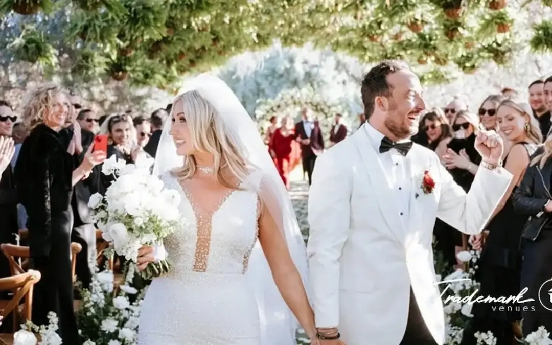 A bride and groom smiling with their wedding party outdoors at a Trademark Venues location in Southern California.
